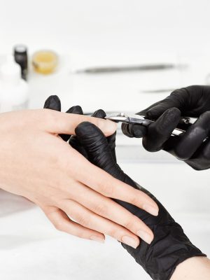 Professional manicurist in black gloves provides service to client making manicure with manicure cuticle trimmer.